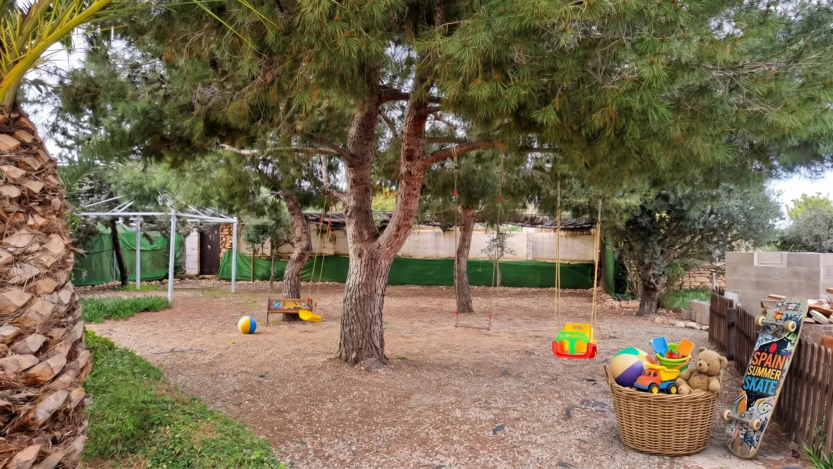 Parque infantil privado con columpios bajo los pinos en el jardín vallado de la casa rural
